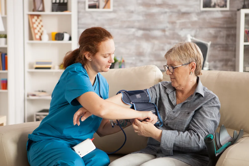 Caregiver assisting an elderly man with medication in a sunlit living room